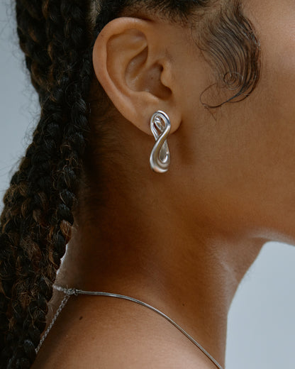 Close-up of a person wearing a silver infinity symbol earring with a blurred background