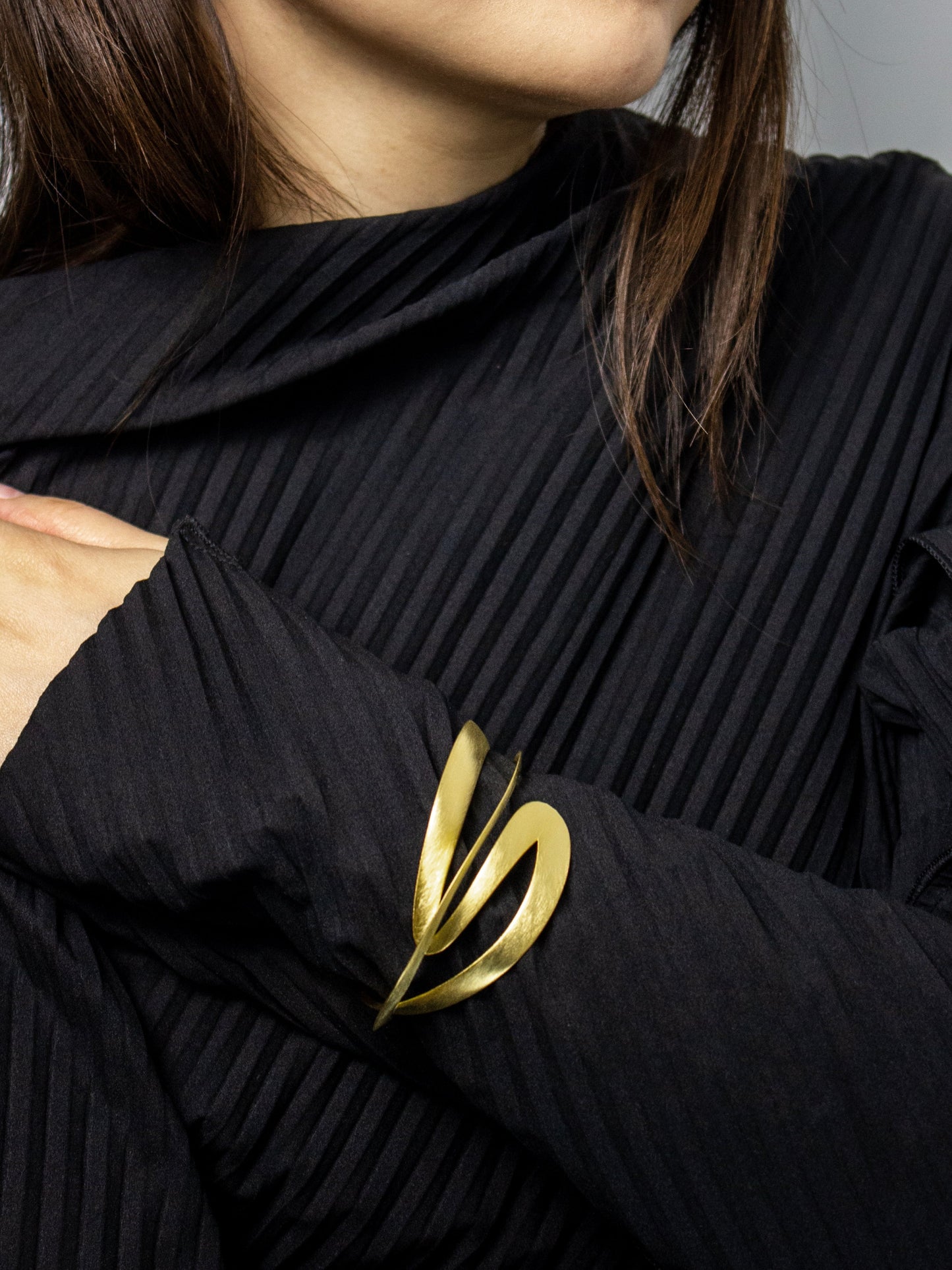 Close-up of a person wearing a black pleated garment with a gold sculptural bangle.