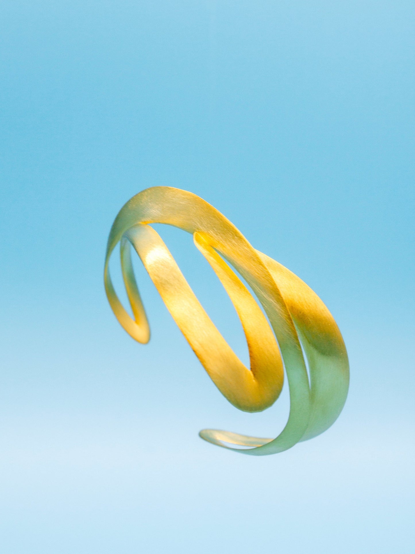 Contemporary sculptural Gold bracelet with hand craft finishing texture floating on a light blue sky