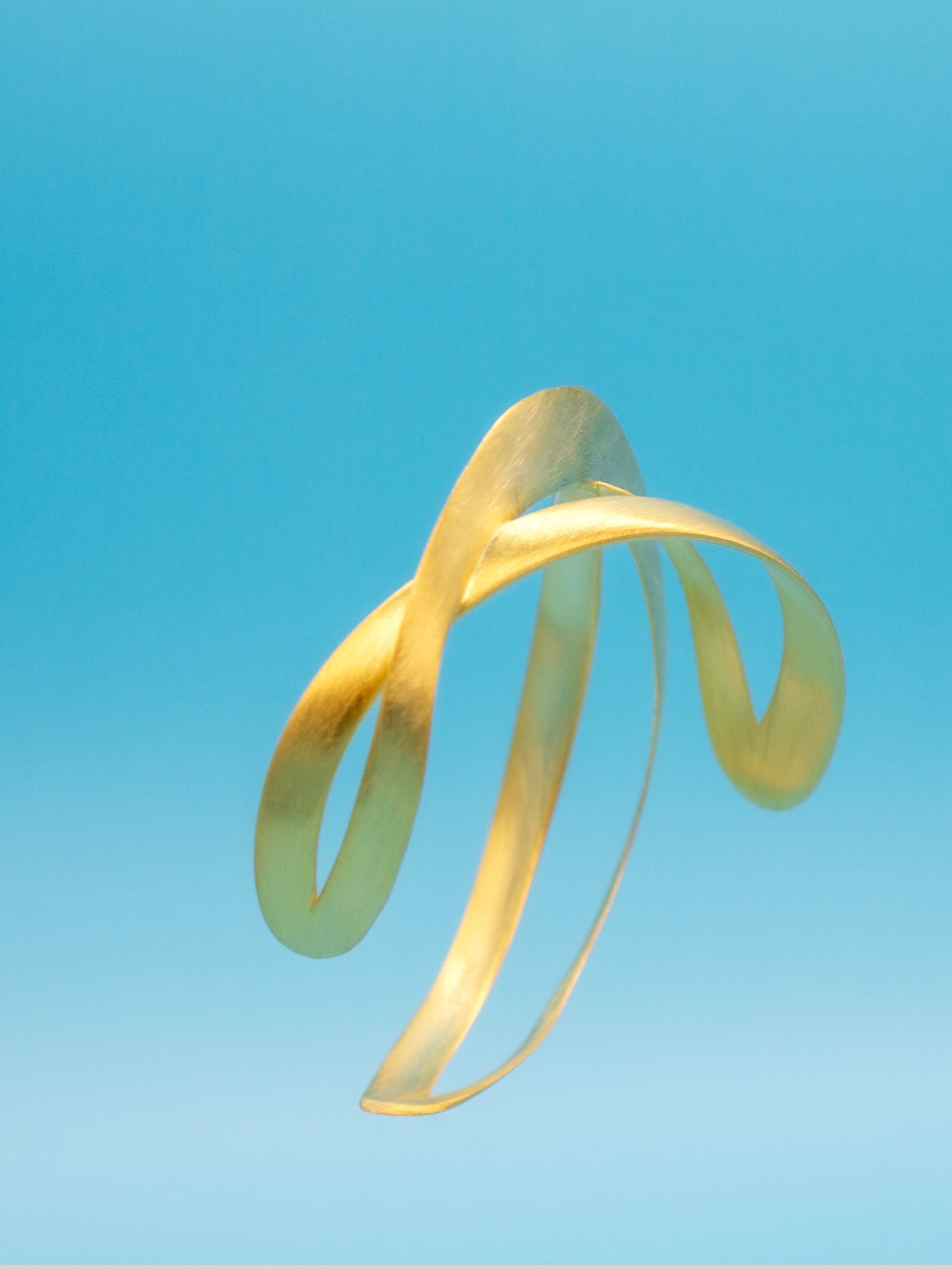 Fluid 3D shaped Gold bracelet on a blue background