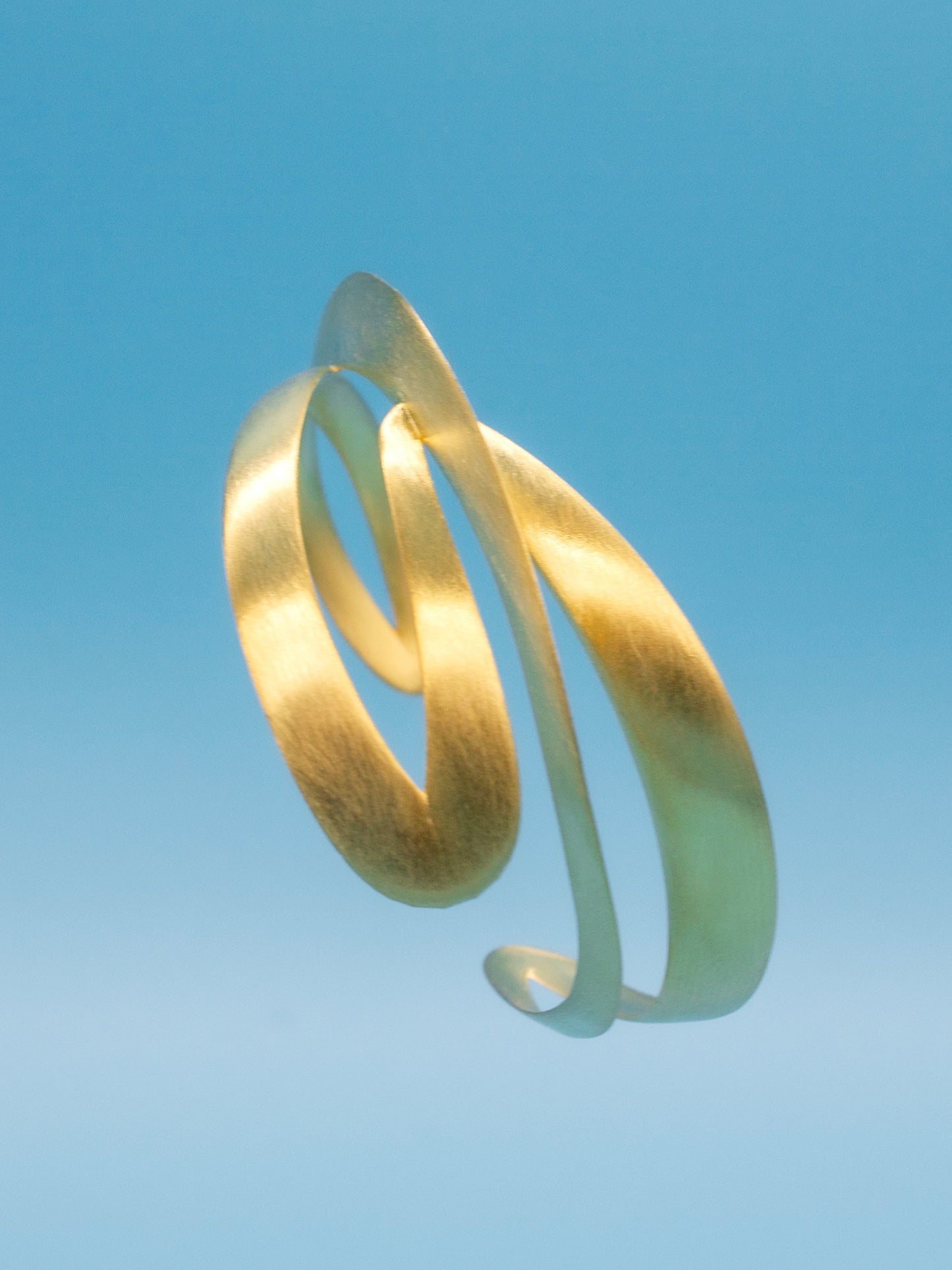 3D dynamic contemporary gold spiral bracelet against a clear blue sky