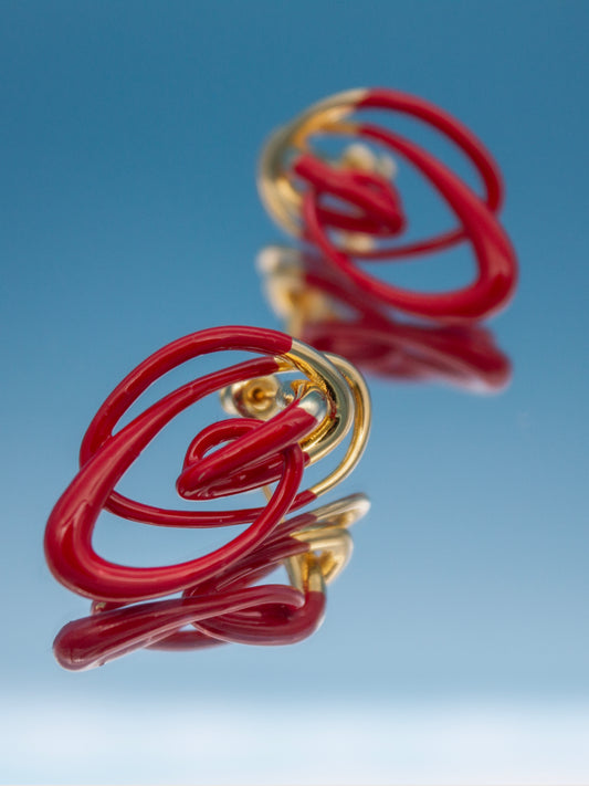 Independent designer statement earrings in glossy red and gold, abstract sculptural drop earrings shown on ear and in flat lay, contemporary art jewelry and niche designer accessories for those seeking unique, wearable sculpture.