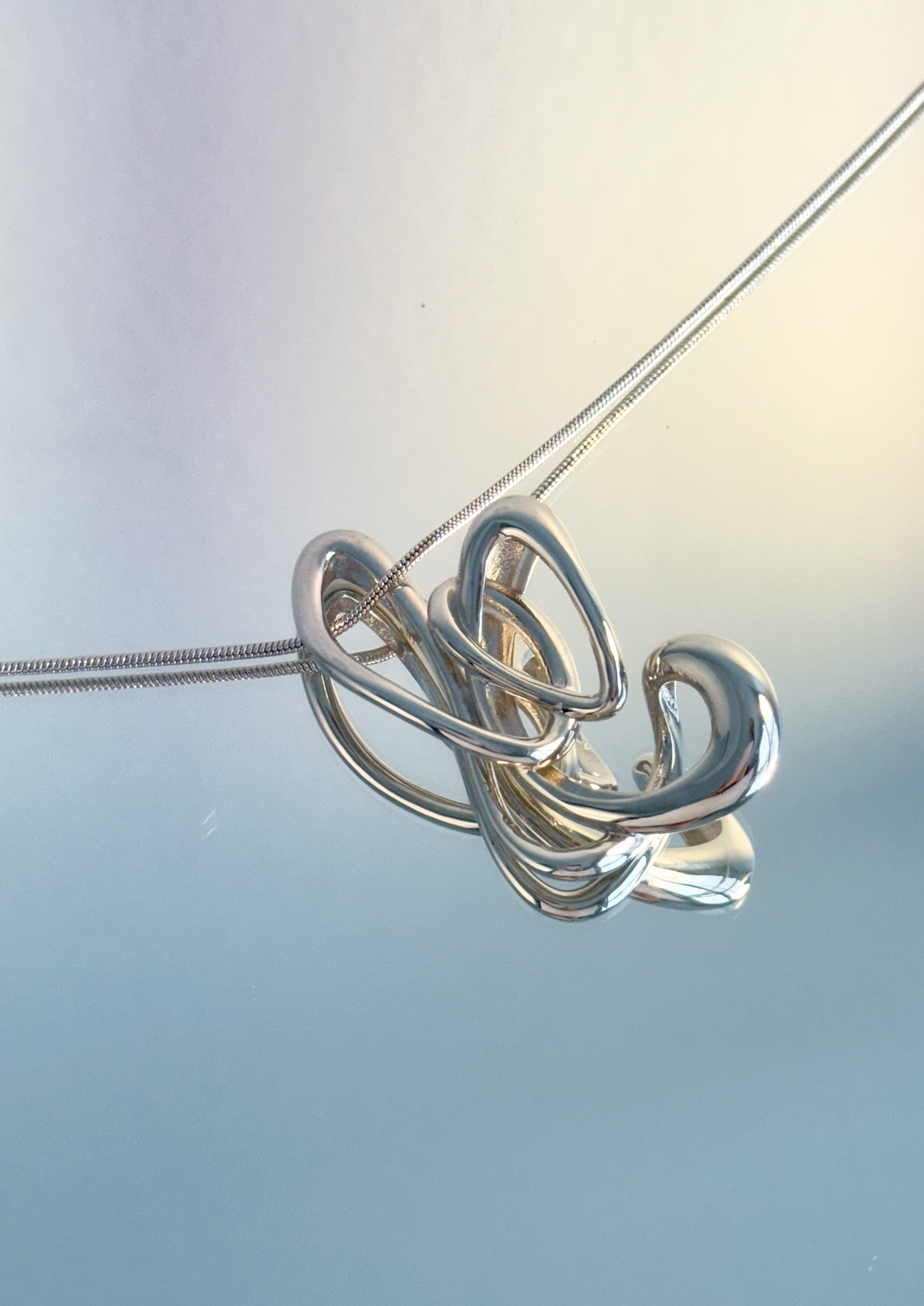 Futuristic looking 3D printed butterfly like pendant on a blue background