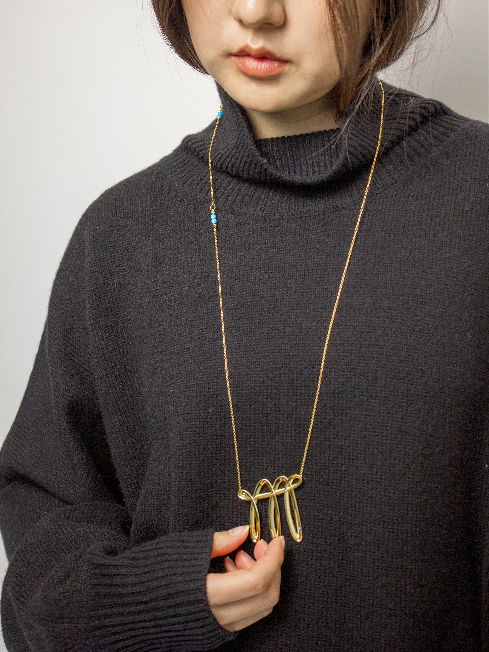 Person wearing a dark sweater with a long gold necklace