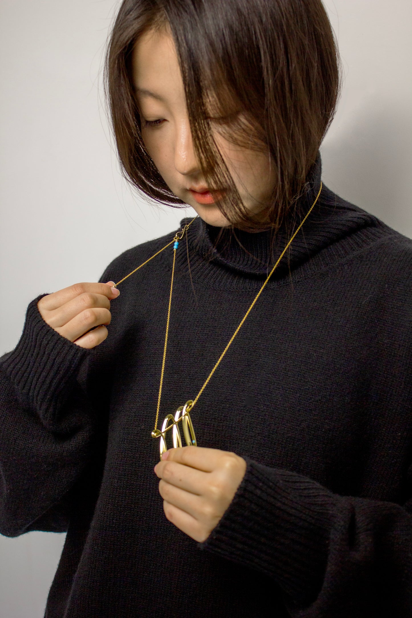 Person wearing a dark sweater and gold necklace with an adjustable details. 