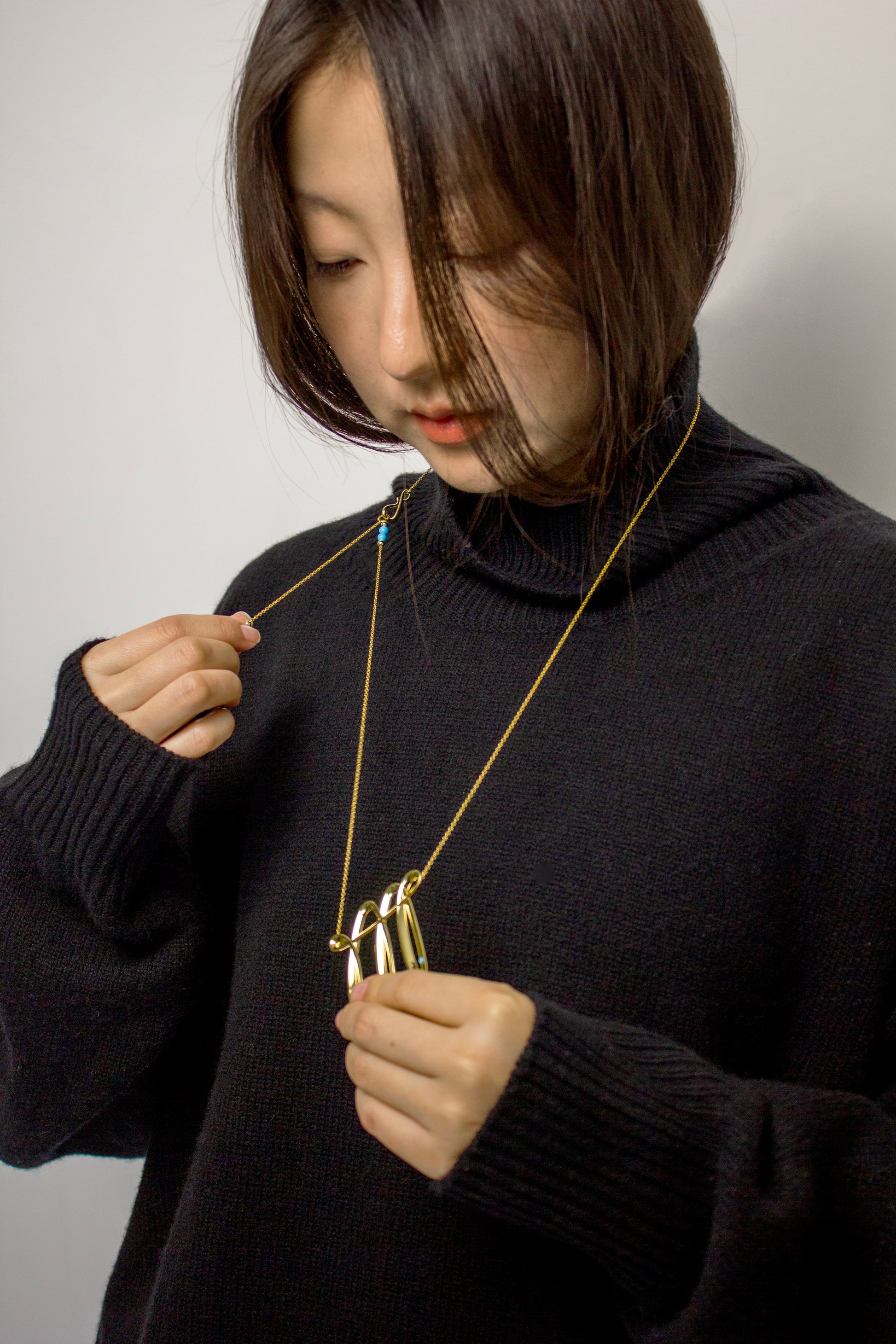 Person wearing a dark sweater and gold necklace with an adjustable details. 