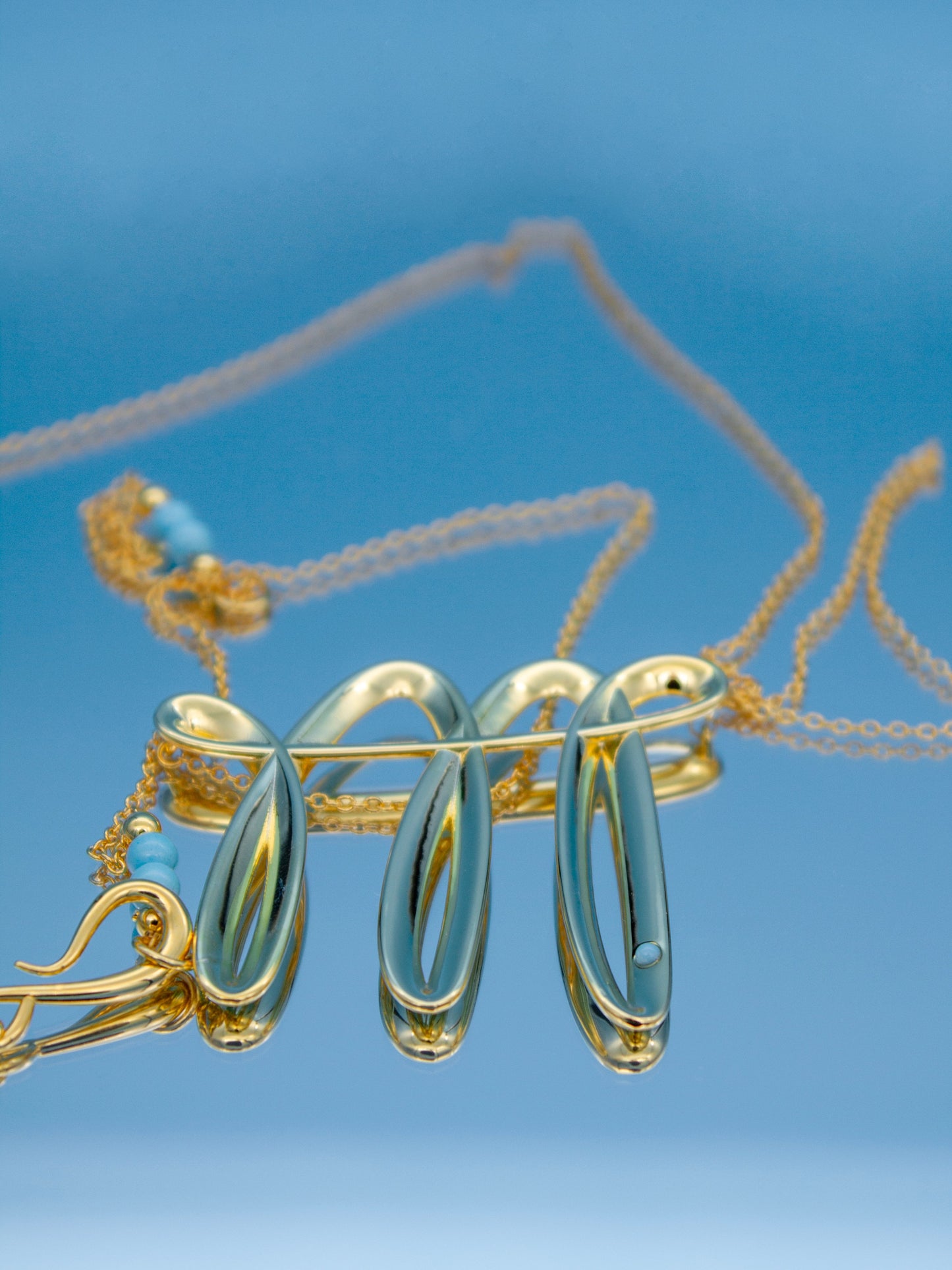 Gold necklace with a contemporary 3D stroke pendant against a blue background