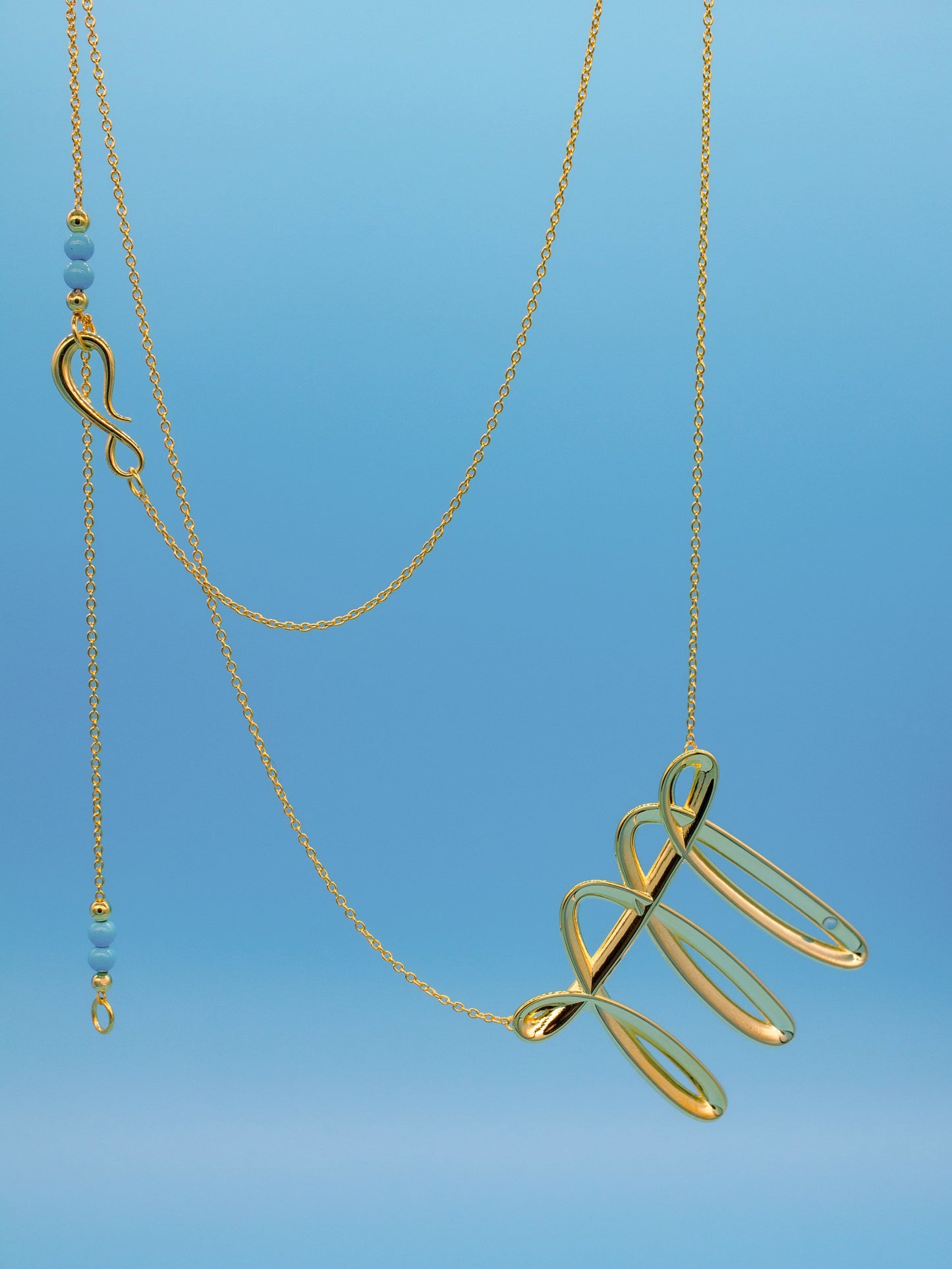 Gold necklace with an interesting fluid stroke like pendant on a blue background