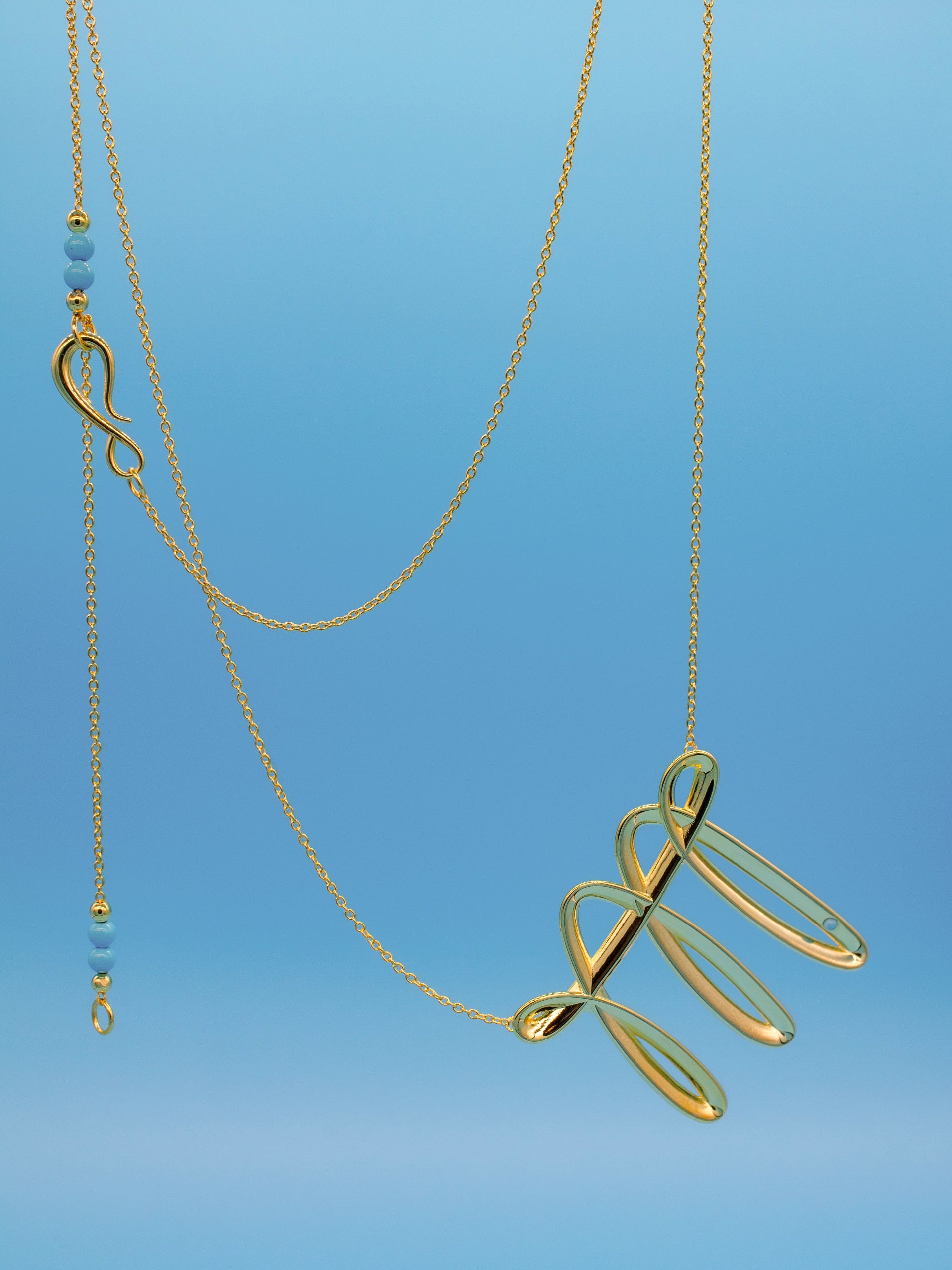 Gold necklace with an interesting fluid stroke like pendant on a blue background