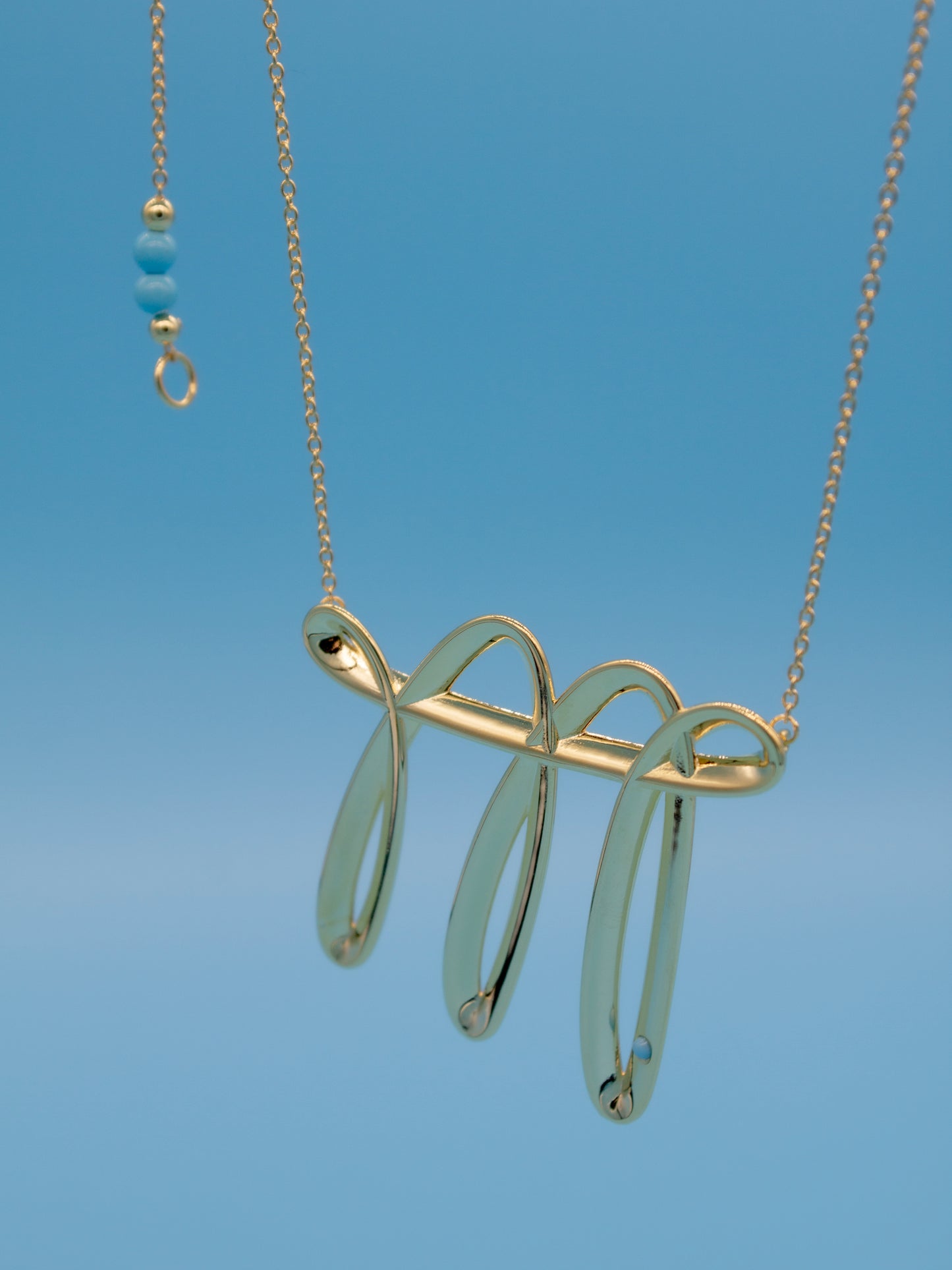 Gold necklace with a doodling like contemporary pendant against a blue background
