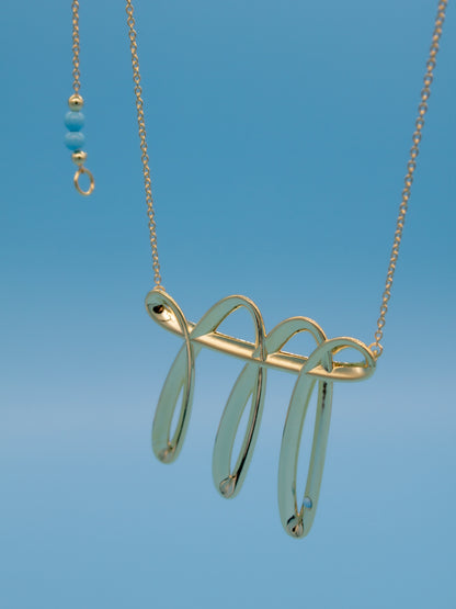 Gold necklace with a doodling like contemporary pendant against a blue background