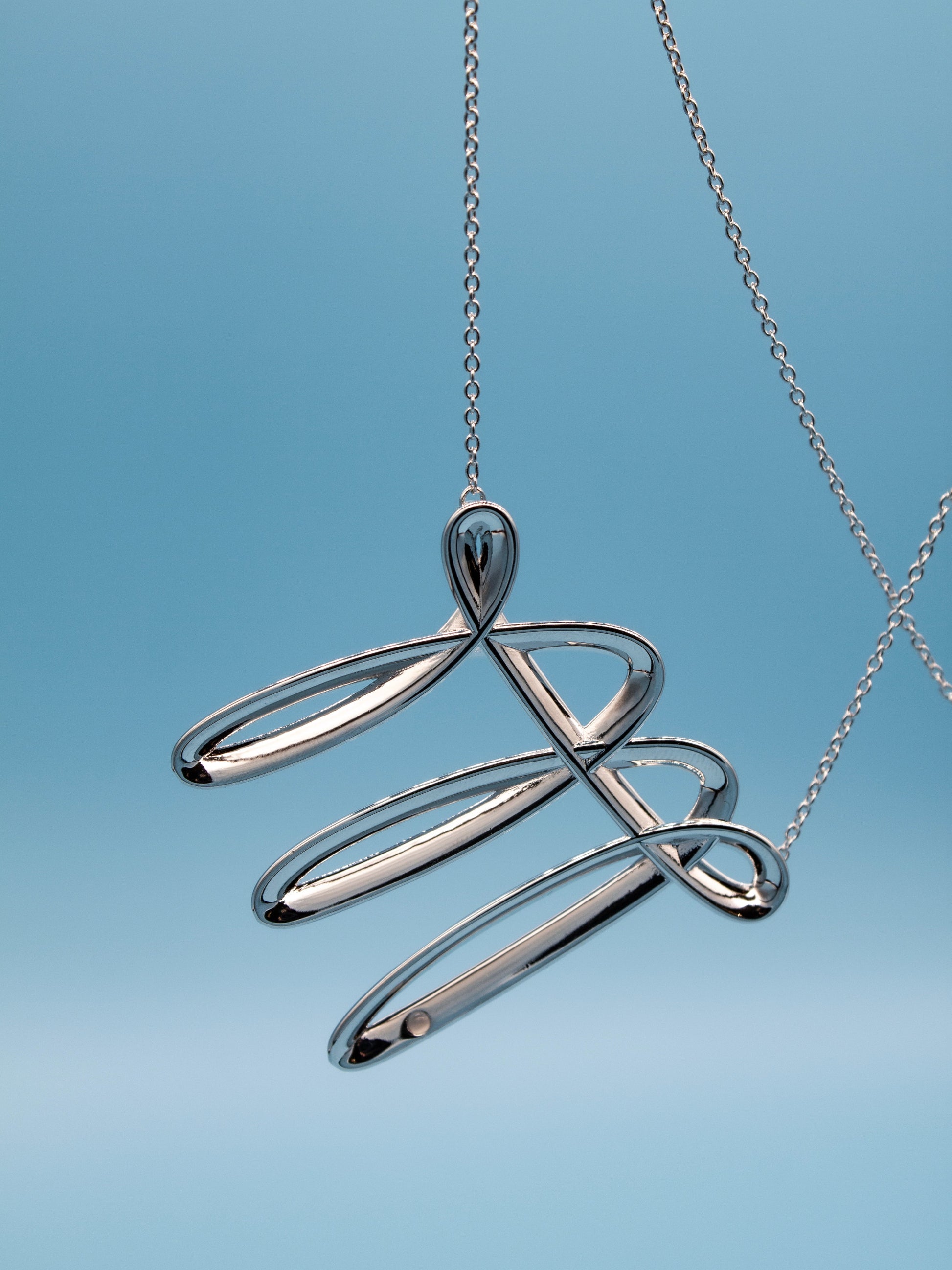 Silver necklace with a stroke like pedant with a cat eye stone on a light blue background