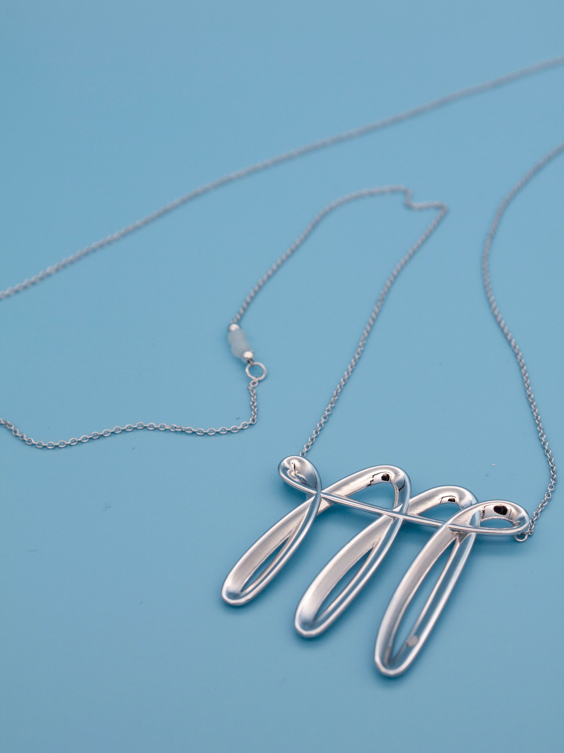 featuring a flowing sculptural pendant, cat eye accents, adjustable extension chain, and custom S-hook clasp