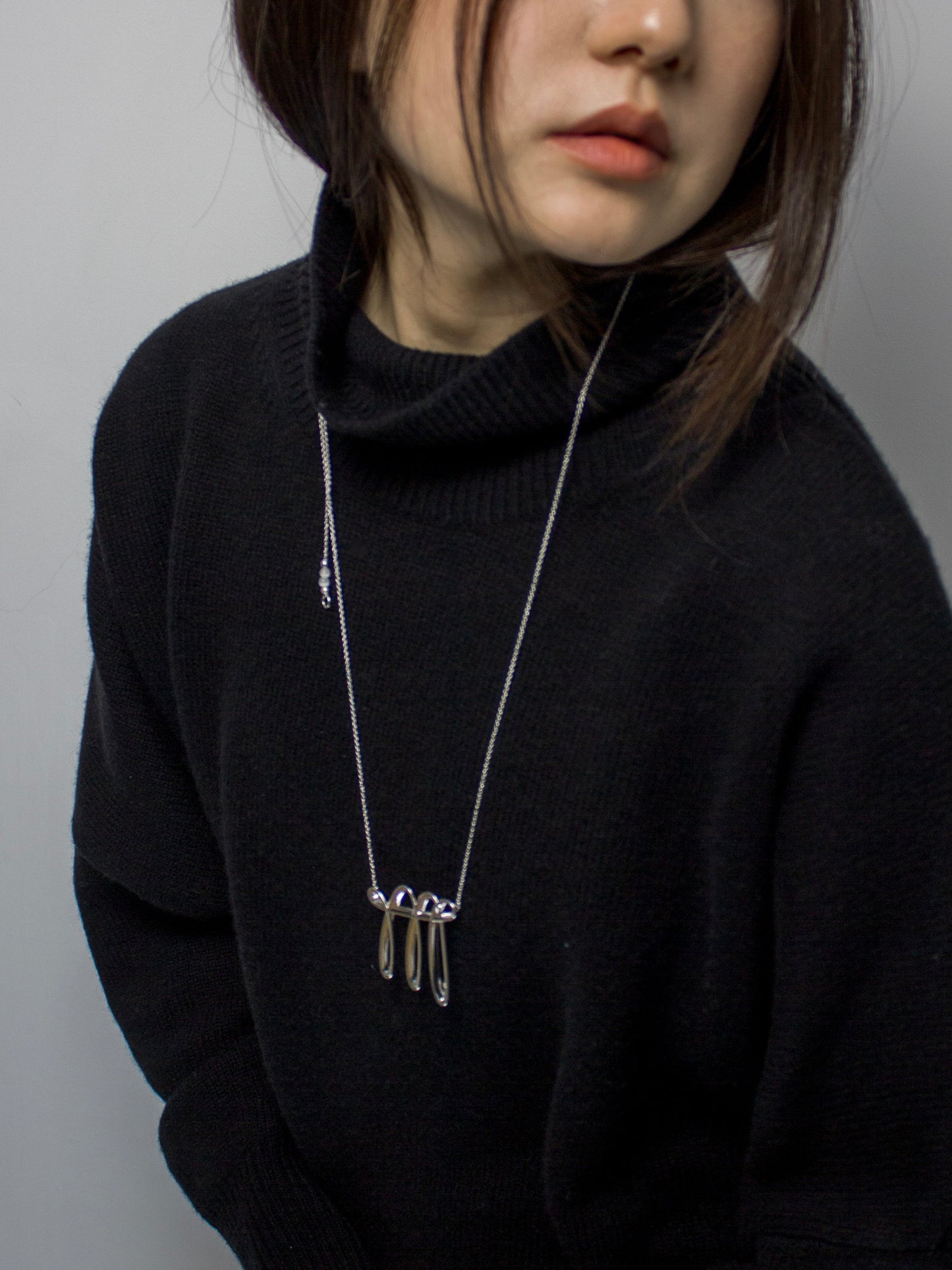 Person wearing a black sweater with a long cool silver necklace.