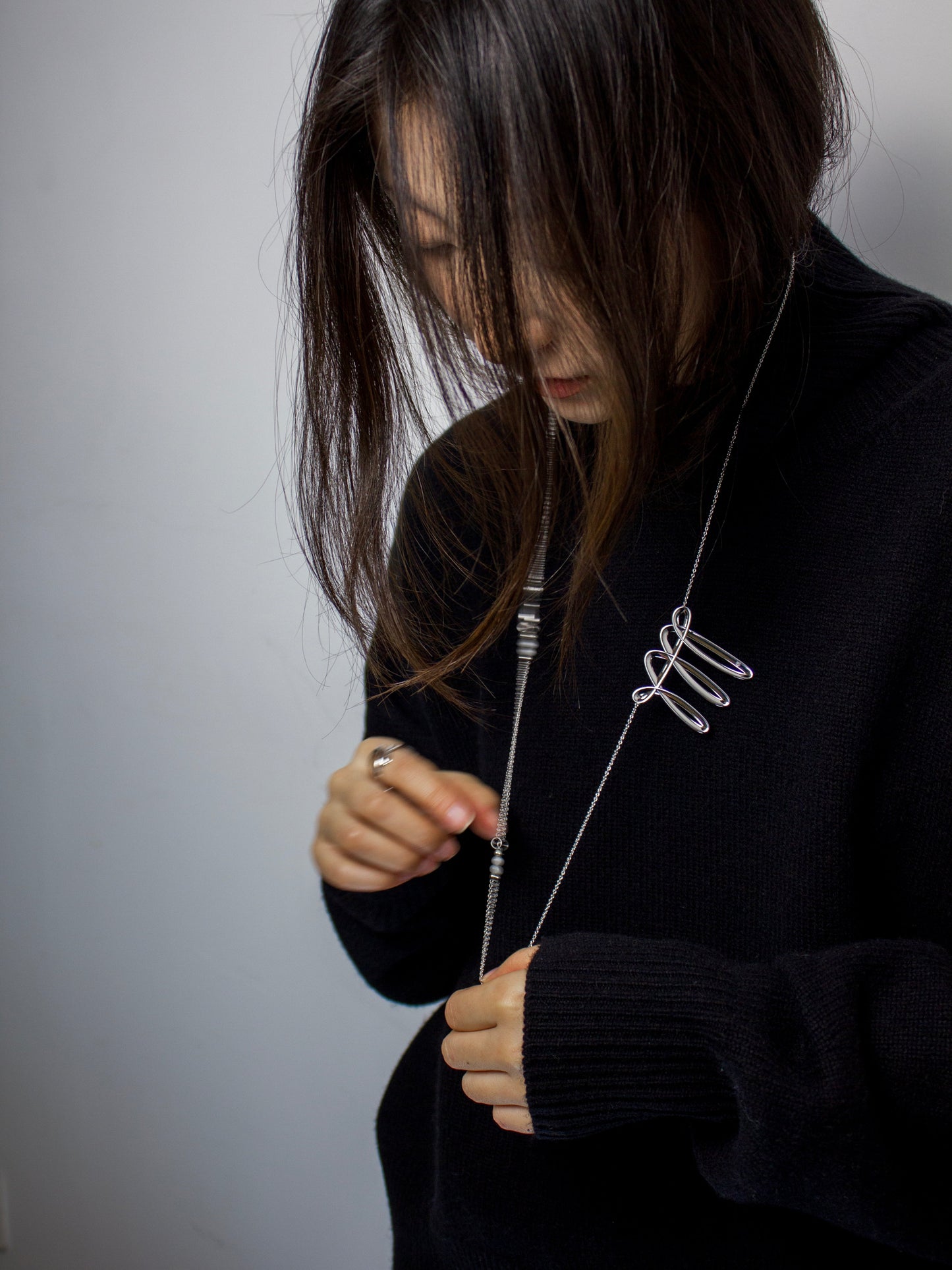 Person wearing a black sweater holding a silver necklace with a contemporary design.