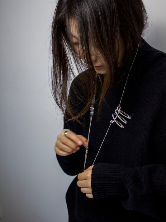 Person wearing a black sweater holding a silver necklace with a contemporary design.