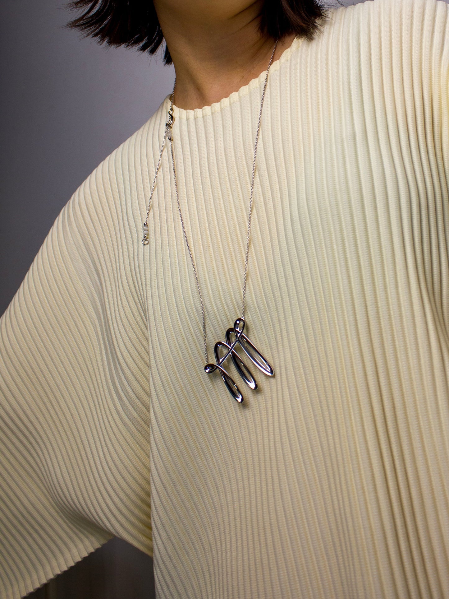 Person wearing a 3D printing technology driven necklace with a minimal designed pendant on a plain background